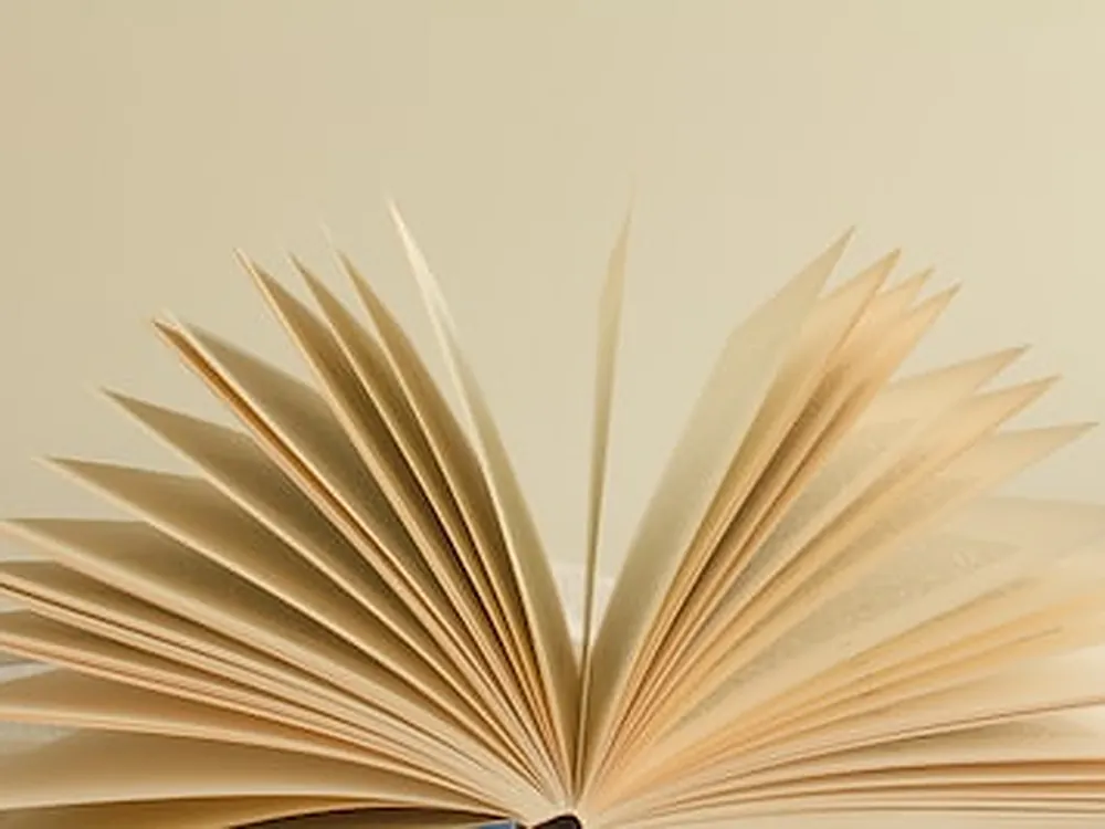 Livre ouvert dont les pages se déploient en éventail, sur un fond beige clair.