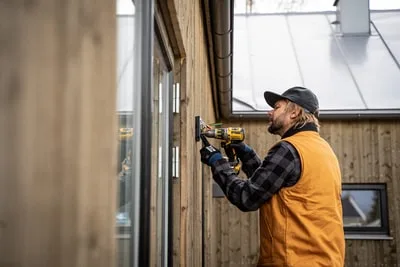 Électricien avec gants de travail qui installe une boîte électrique dans un mur.