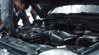 Mécanicien en uniforme gris penché sur le moteur d'une voiture, capot ouvert